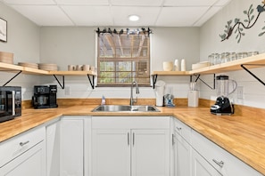A modern kitchen with white cabinets, a stainless steel sink, and wooden countertops.