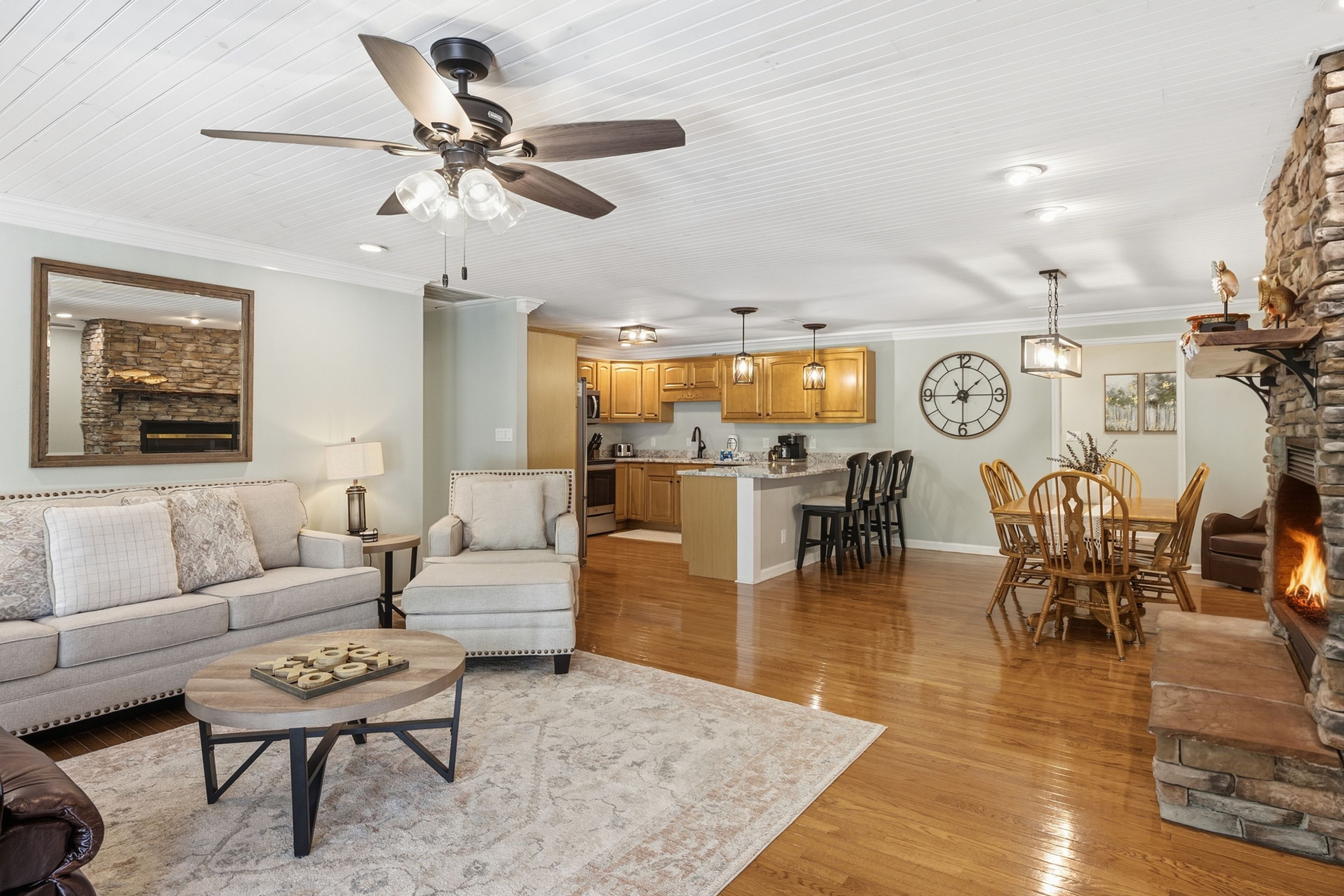 A spacious living room with a fireplace, a dining area with wooden chairs, a kitchen with wooden cabinets, and a ceiling fan.