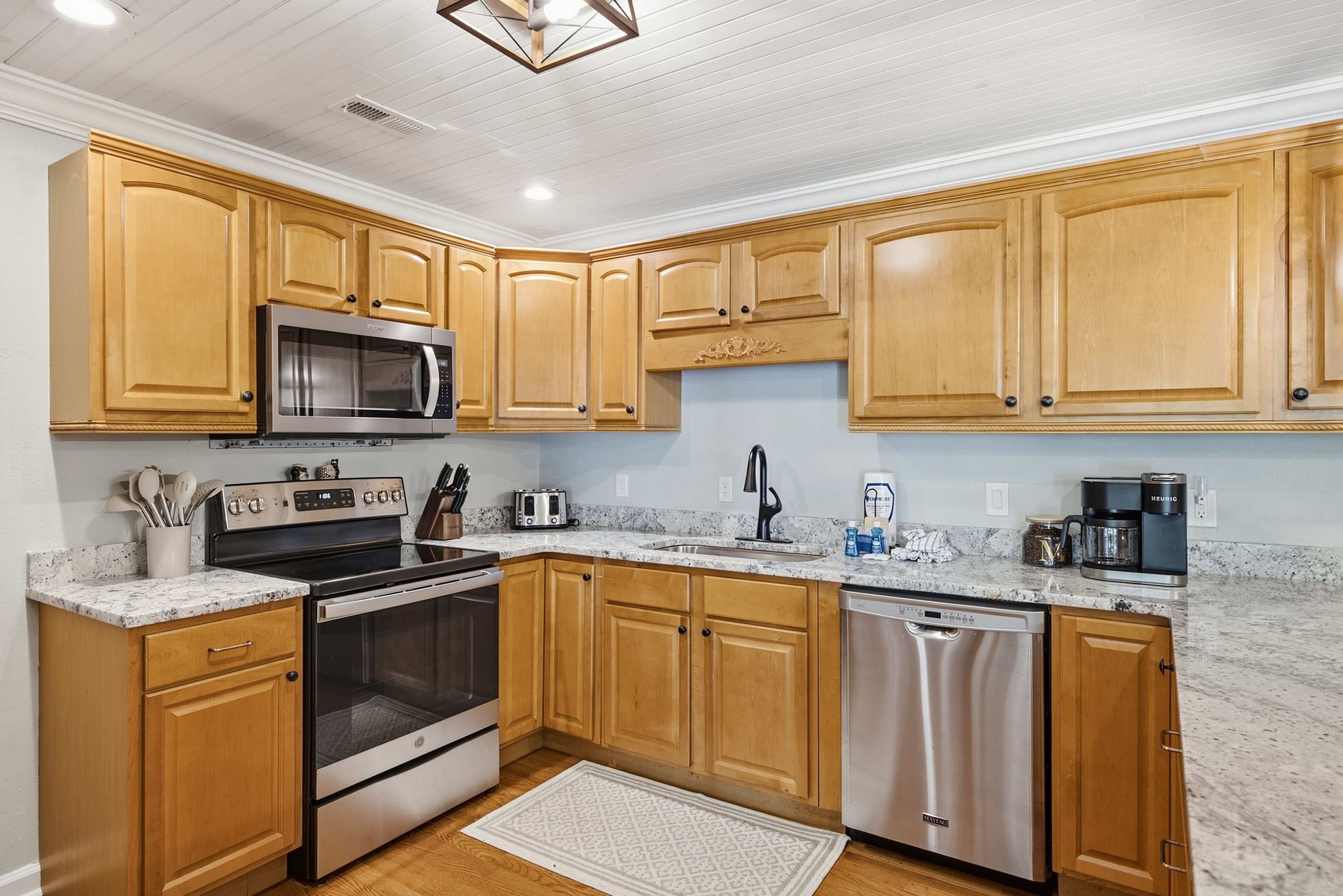 A modern kitchen with wooden cabinets, stainless steel appliances, a granite countertop, and a built-in dishwasher.