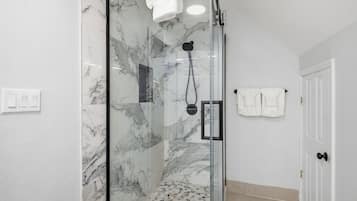 A glass-enclosed shower with marble walls, a white towel hanging on the wall, and a door with a towel rack.