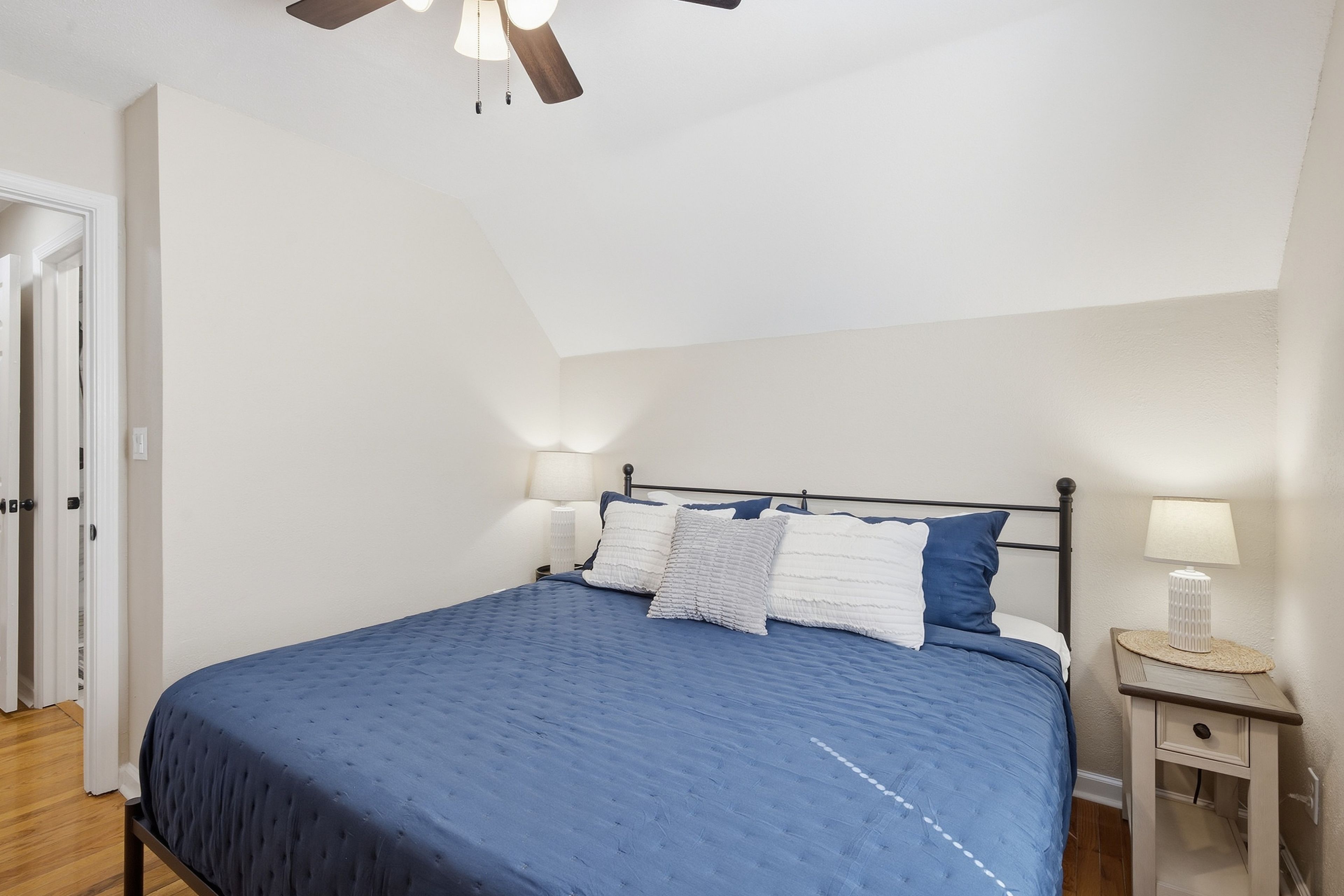 A bedroom with a bed, bedside lamps, a nightstand, and a ceiling fan.