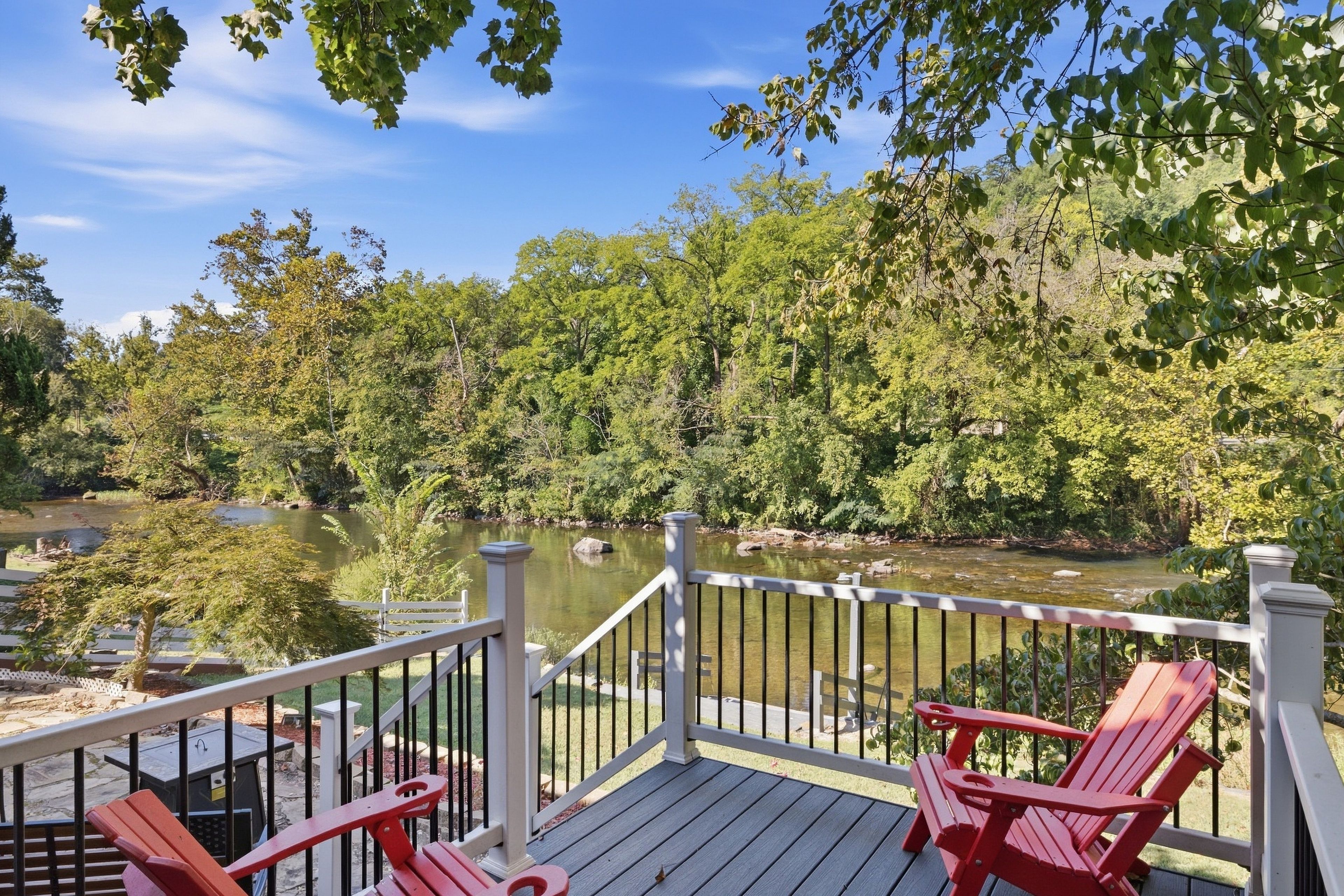A deck with a railing overlooking a river and forest.