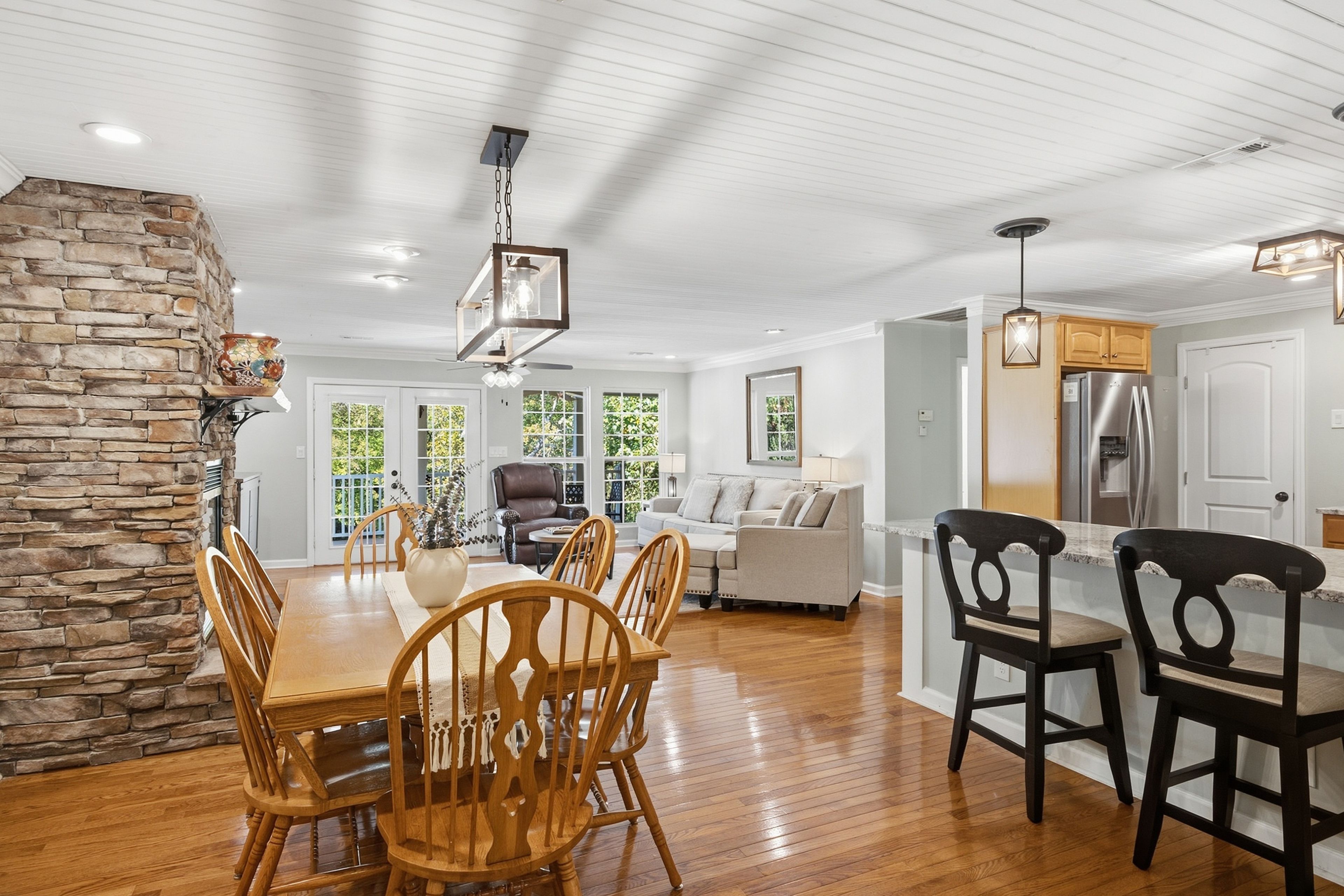 A spacious living area with a dining table, chairs, a stone accent wall, and a kitchen with modern appliances.
