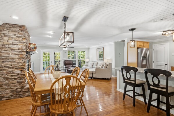 A spacious living area with a dining table, chairs, a stone accent wall, and a kitchen with modern appliances.