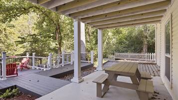A covered outdoor deck with a picnic table and red Adirondack chairs.