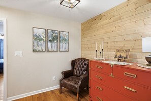 A room with a wooden wall panel, a brown leather chair, a red dresser with drawers, and three framed paintings on the wall.