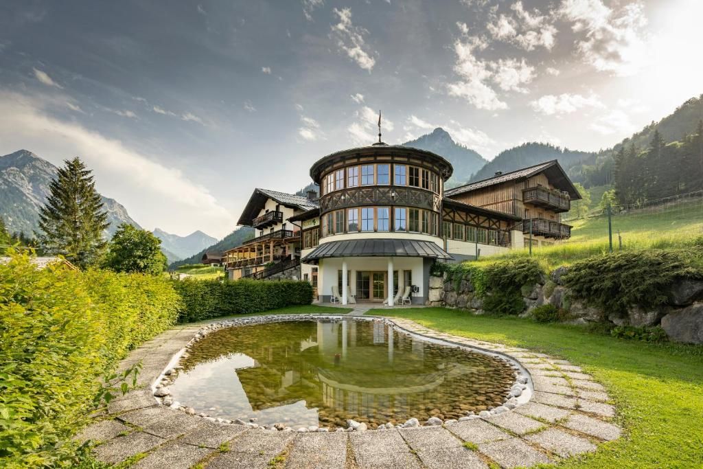 Ein Chalet-Stil Gebäude mit einem runden, zentralen Turm, umgeben von einem gepflegten Garten und einem Teich.