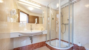 A modern bathroom with a glass-enclosed shower, a sink with a vanity, and a mirror. - Gasthof Kleefeld (Strobl)