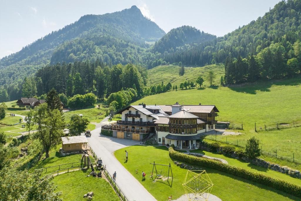 Ein großes, mehrgeschossiges Gebäude mit einem markanten Mittelbau und einem kleineren Anbau zur Linken. Vor dem Gebäude erstreckt sich eine gepflegte Grünfläche, und eine Straße führt zum Eingang.