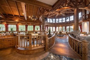 A spacious wooden interior with a high ceiling, multiple dining areas, and a central stone feature. - Gasthof Kleefeld (Strobl)