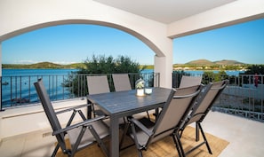 A balcony with a table and chairs, overlooking a body of water and a hilly landscape. - Villa Laron (Bilice)