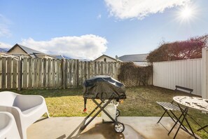 A backyard with a barbecue grill, a white plastic chair, a metal table, and a wooden fence. - Apollo Hideaway | Self-Contained 1-Bedroom Retreat, Full Kitchen & Easy Access to Wānaka (Wānaka)