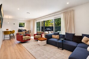 A modern living room with a sofa, chairs, a coffee table, and a dining area with a table and chairs. - Modern Wānaka Retreat | 4 Bedrooms, Sleeps 8, Hot Tub, 2 Living Areas & Balcony (Wānaka)