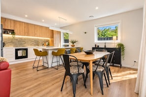 A modern kitchen with wooden cabinets, a central island, and a dining area with a wooden table and chairs. - Modern Wānaka Retreat | 4 Bedrooms, Sleeps 8, Hot Tub, 2 Living Areas & Balcony (Wānaka)