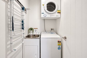 A compact laundry room with a washing machine, a dryer, and a metal drying rack. - our Wānaka Base | Sleeps 6, 3 Bedrooms, Mountain Views, Pool, Spa, Gym & Tennis Court (Wānaka)