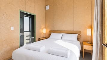A hotel room with a large bed, two bedside tables with lamps, a wooden headboard, and a door leading to a bathroom.