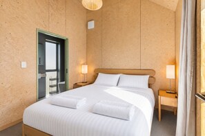 A hotel room with a large bed, two bedside tables with lamps, a wooden headboard, and a door leading to a bathroom.