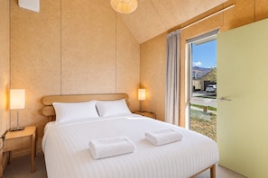 Ein Hotelzimmer mit einem Bett, zwei Nachttischlampen, einem Vorhangfenster und Blick ins Freie.