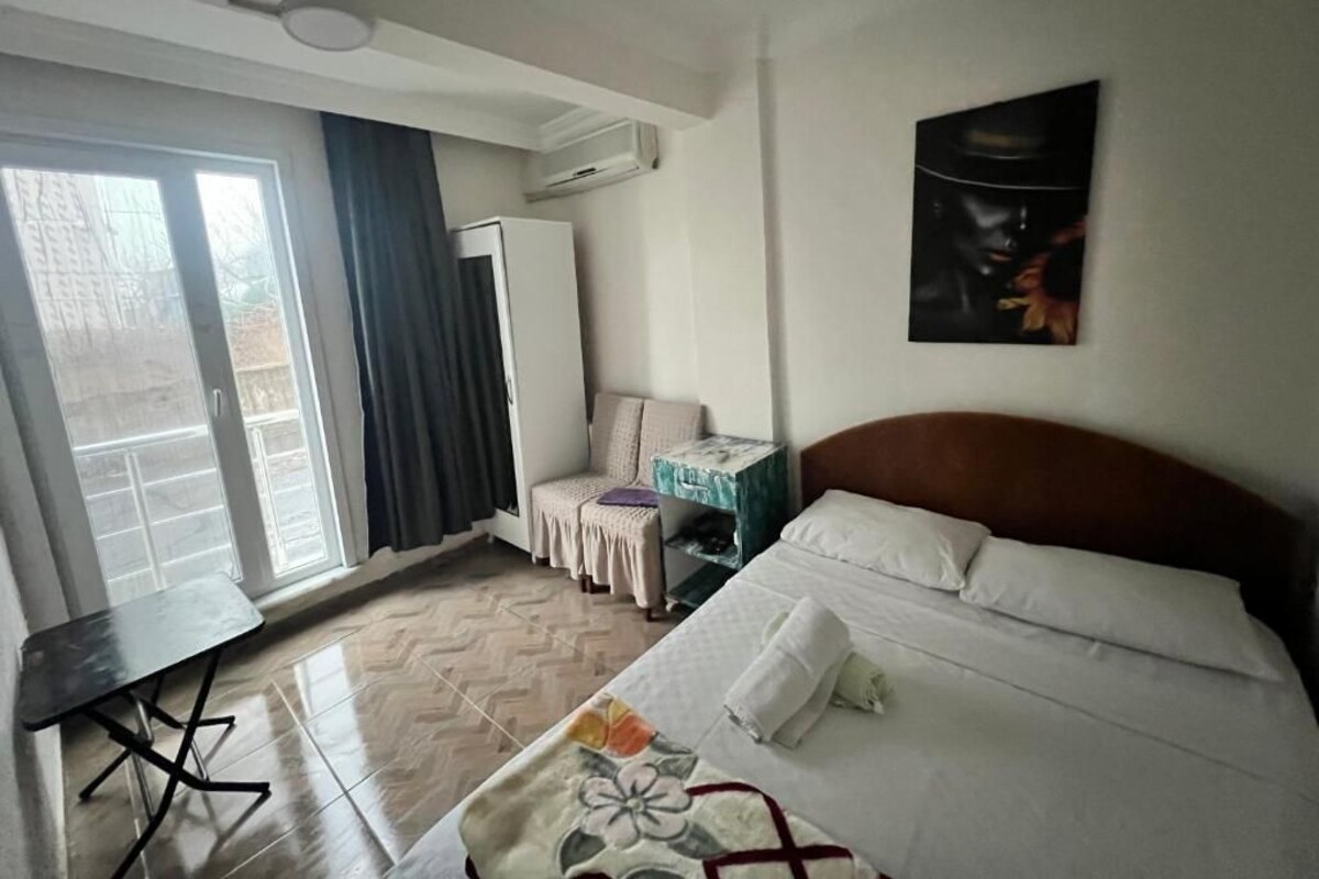 Hotellihuone, jossa on sänky, työpöytä, tuoli, vaatekaappi ja suuri ikkuna.