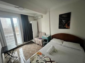 Hotellihuone, jossa on sänky, työpöytä, tuoli, vaatekaappi ja suuri ikkuna.