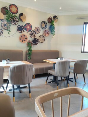 A modern dining area with a long table, cushioned seating, and decorative woven baskets on the wall.