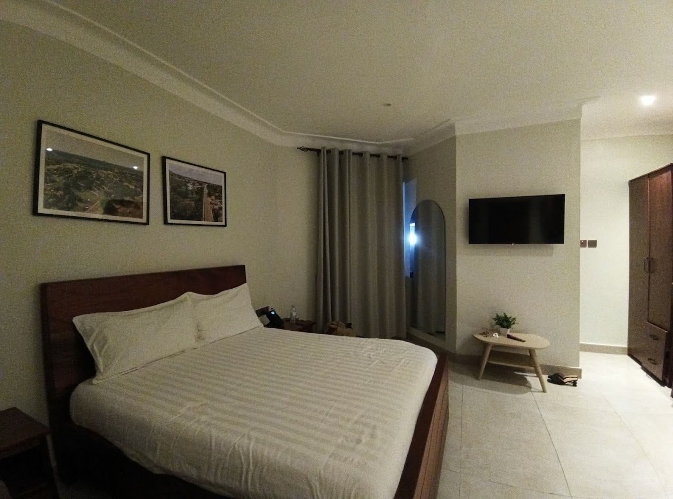 A hotel room with a bed, a flat-screen TV, a small table, and a mirror.