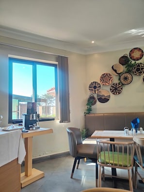 Un comedor con una mesa, sillas, una cafetera y un ventanal con cortinas.