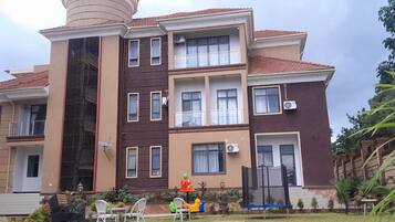 Un edificio residencial de varios pisos con balcones, unidades de aire acondicionado y una pequeña zona de estar al aire libre con sillas y una mesa.