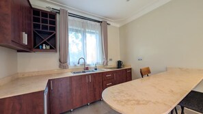 A compact kitchen with a sink, a window with curtains, a countertop, and a dining table.