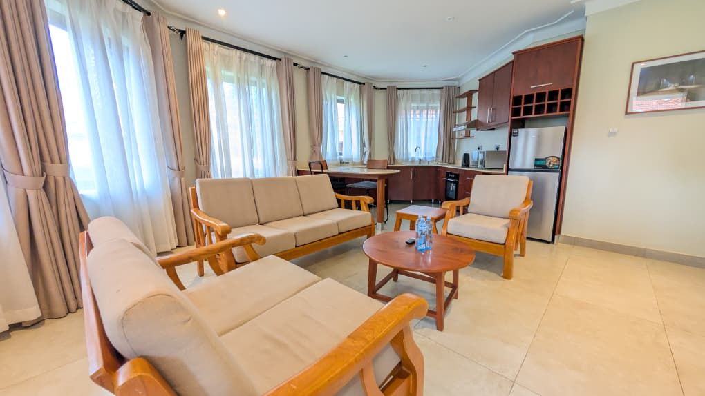 Sala de estar com sofá, cadeiras, mesa de centro e área de cozinha ao fundo.