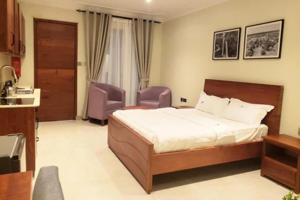 A bedroom with a wooden bed, a desk, a chair, a wardrobe, and a bathroom.
