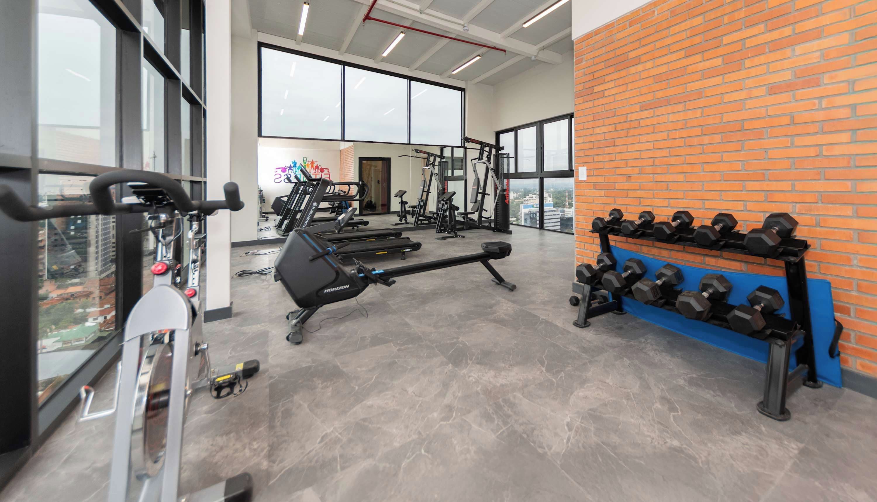 Un gimnasio con equipo de ejercicio, una banca y mancuernas.