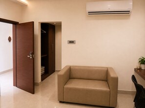 A room with a beige sofa, a wooden door, a closet, and a wall-mounted air conditioner. - Hotel Element Stay By OTABoostup  (Hyderabad)