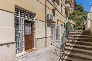 A narrow street with a building featuring a wooden door, a metal gate, and a staircase with a green railing. - Three-room apartment near the Metro station for the Colosseum (Roma)
