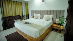 A hotel room with a bed, a small bedside table, a chair, and a potted plant. - Hotel Trisha (Gurugram)