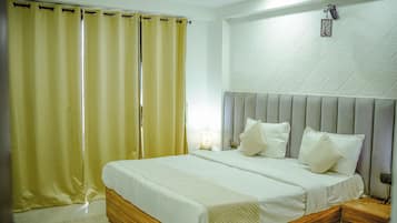 Habitación de hotel con cama, cortinas, mesita de noche y una lámpara fijada a la pared.
