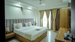 A modern hotel room with a large bed, a bedside table, a desk, and a ceiling fan. - Hotel Trisha (Gurugram)