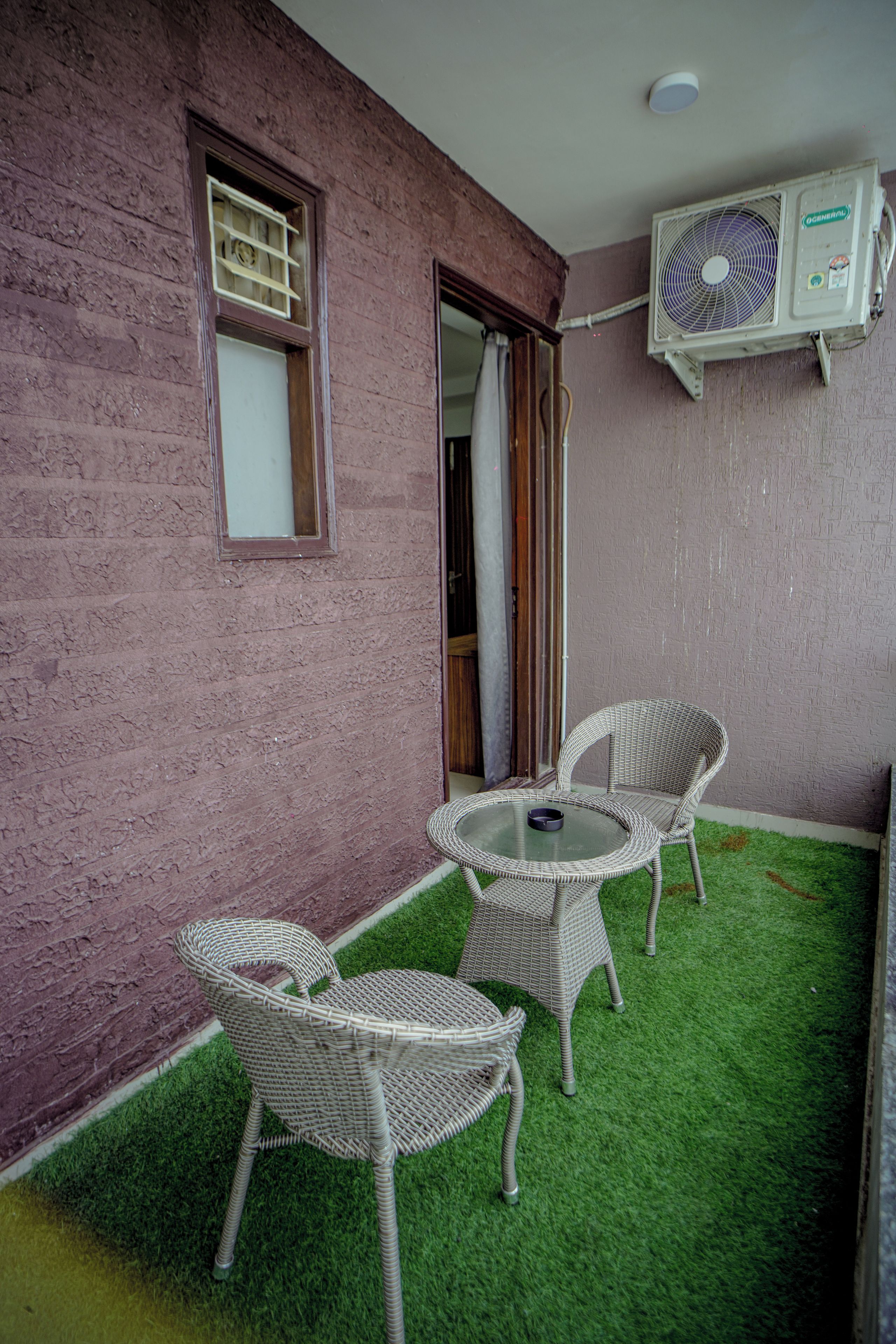 Un patio con una mesa, dos sillas, una mesita redonda y un equipo de aire acondicionado instalado en la pared.