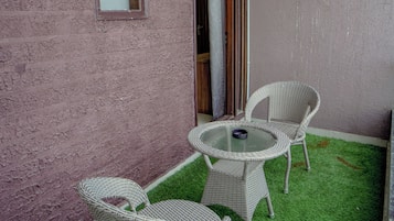 Un patio con una mesa, dos sillas, una mesita redonda y un equipo de aire acondicionado instalado en la pared.