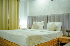 Habitación de hotel con cama, mesita de noche, lámpara de pared y ventana con cortinas.