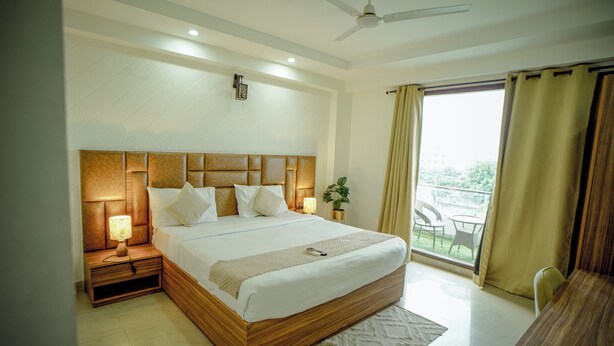 A hotel room with a large bed, bedside lamps, a ceiling fan, and a view of the outdoors. - Hotel Trisha (Gurugram)