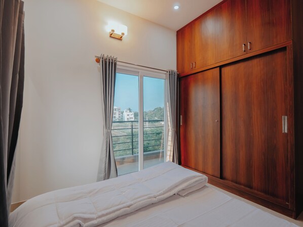 A bedroom with a large window, a wardrobe, and a bed. - Thaswi Service Apartment (Mysore)