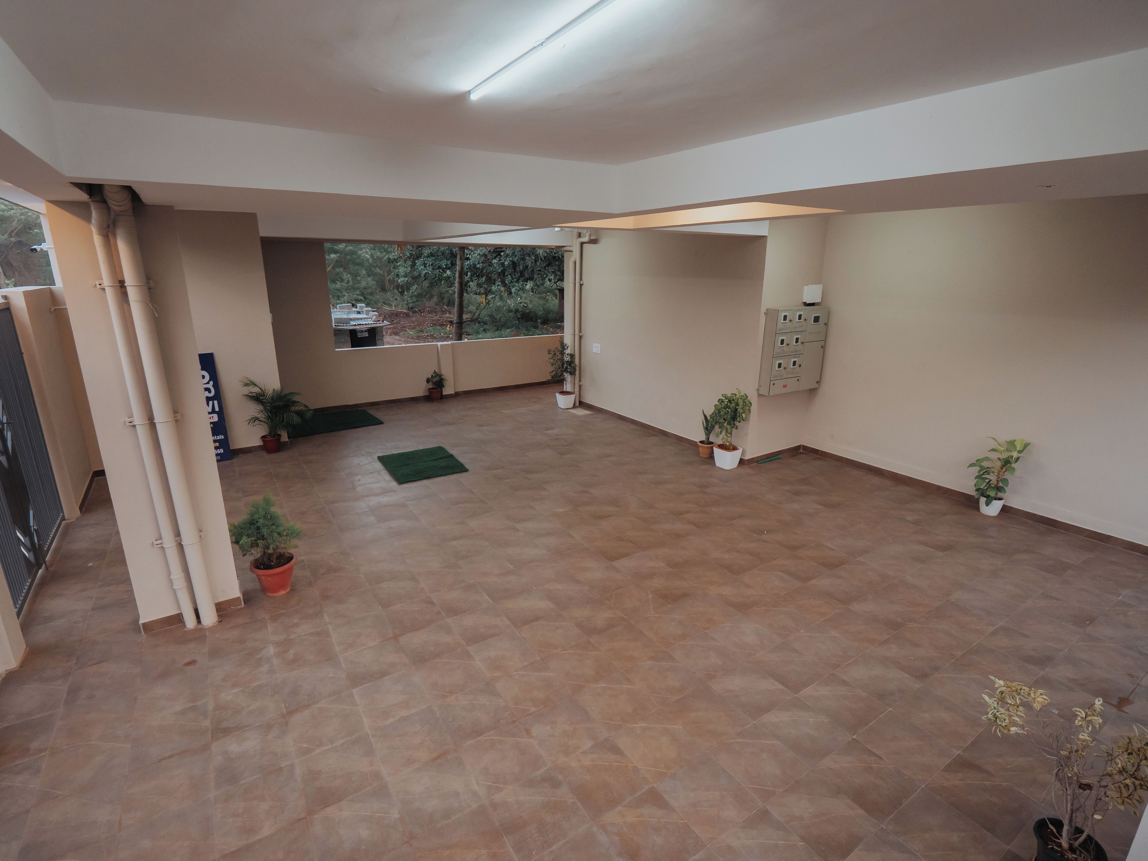 A spacious indoor area with tiled flooring, potted plants, and a view through a glass door.