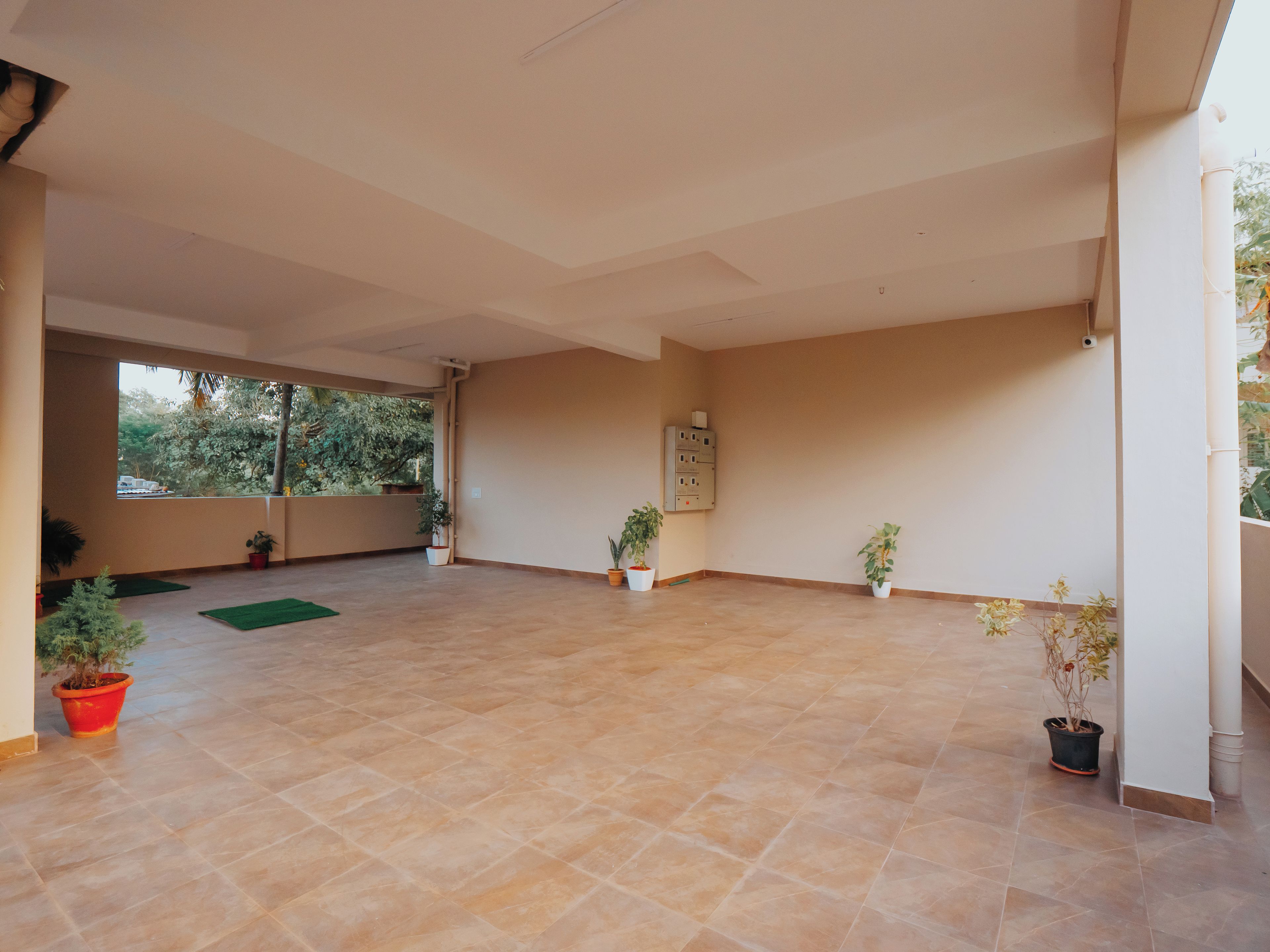 A spacious room with a tiled floor, a large window, and several potted plants.