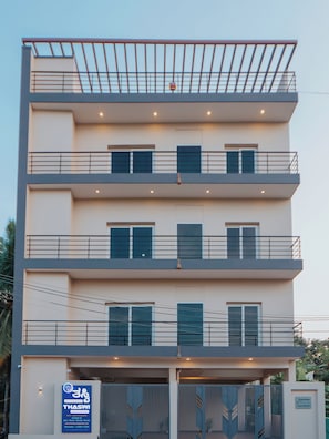 A multi-story building with balconies, a gated entrance, and a sign indicating availability for daily, weekly, monthly, and rentals. - Thaswi Service Apartment (Mysore)