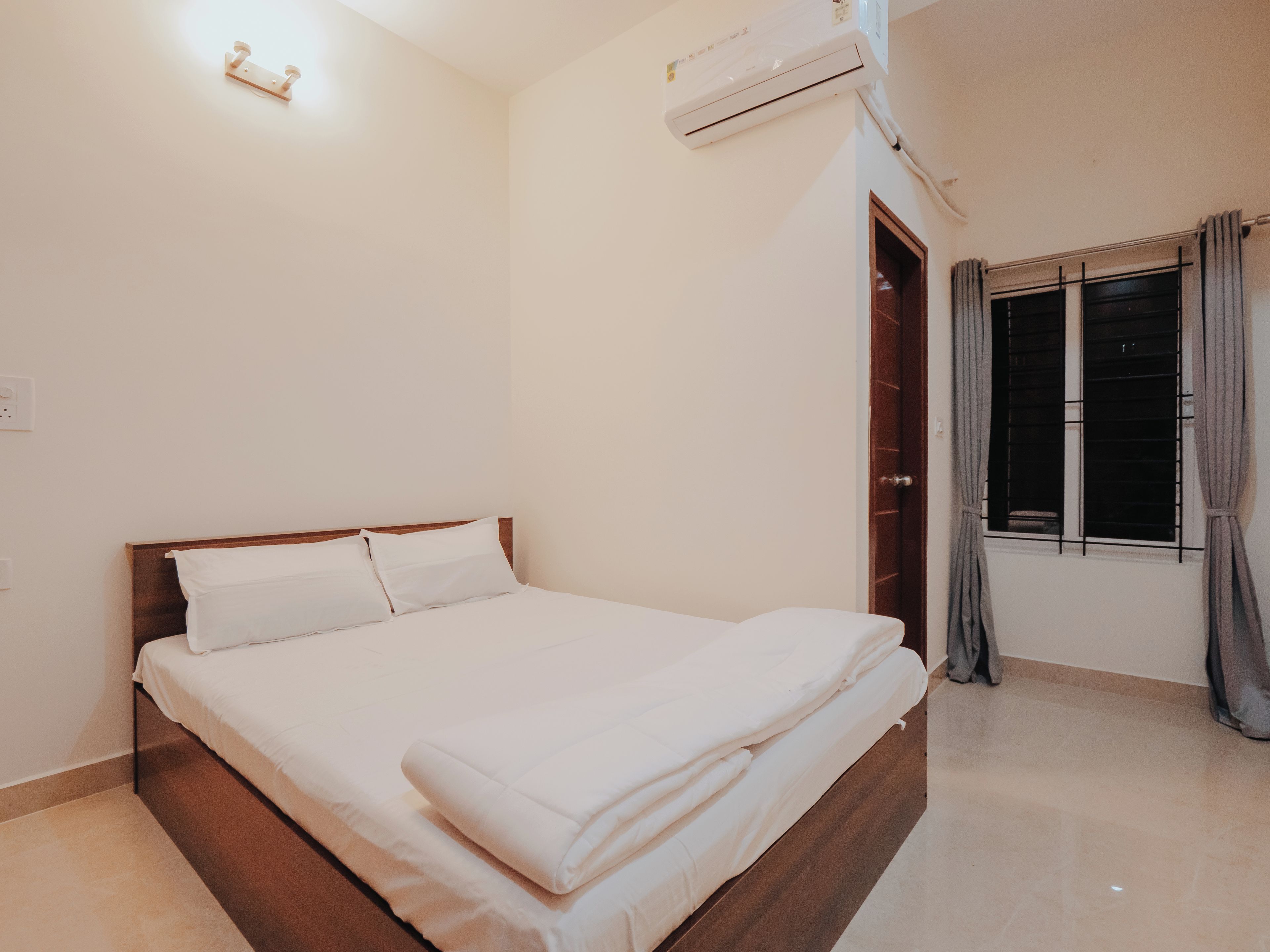 Een net opgemaakt bed in een kamer met een houten hoofdeinde, een raam met gordijnen en een airconditioning op de muur.