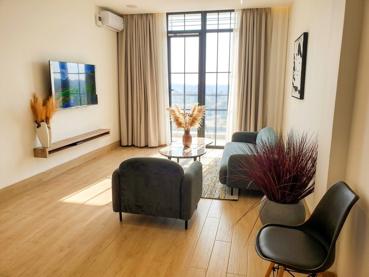 A modern living room with a flat-screen TV, a sofa, a coffee table, and a view through large windows.