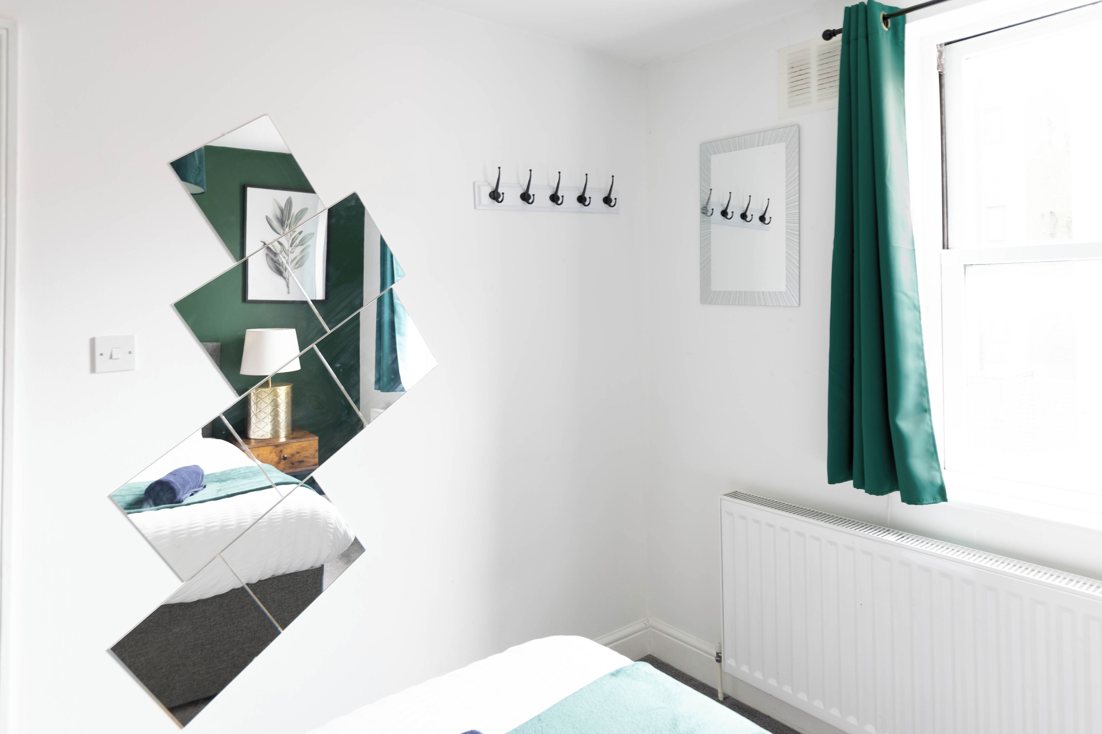 Une chambre à coucher avec un lit, une table de chevet, une lampe, un radiateur et une fenêtre avec des rideaux.