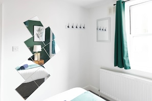 Ein Schlafzimmer mit Bett, Nachttisch, Lampe, Heizkörper und einem Fenster mit Vorhängen.