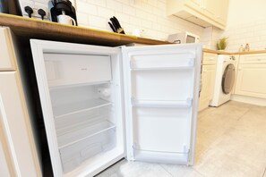 Ein offener Kühlschrank mit mehreren Ablagen, eine Mikrowelle darüber und eine Waschmaschine im Hintergrund.
